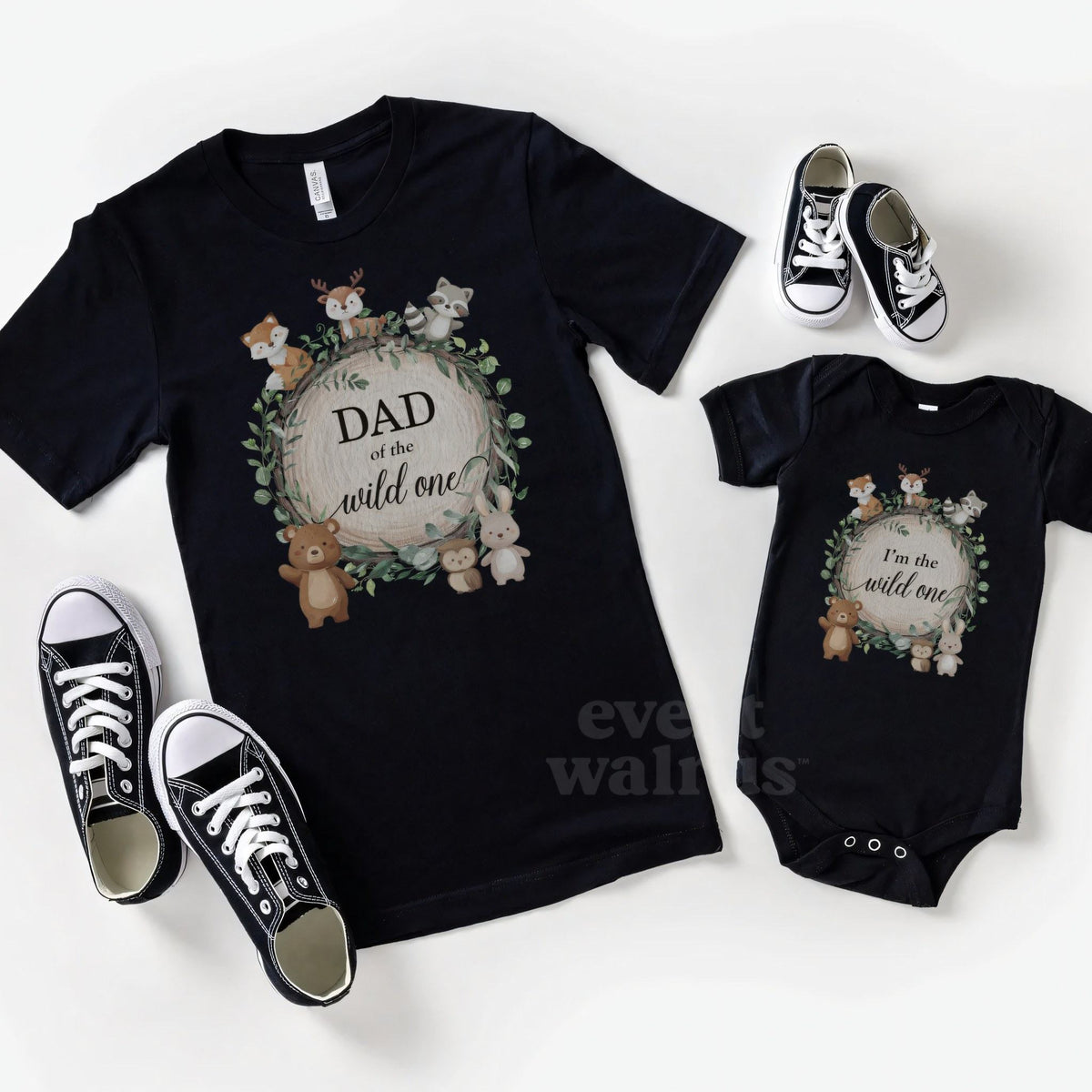 Black Dad of the Wild One shirt and a matching black baby bodysuit laid out with sneakers.