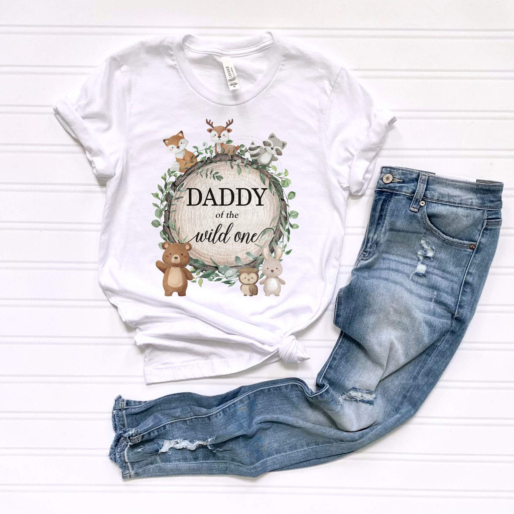 White Daddy of the Wild One adult tee with the fox, deer and bear wreath, laid flat beside jeans.