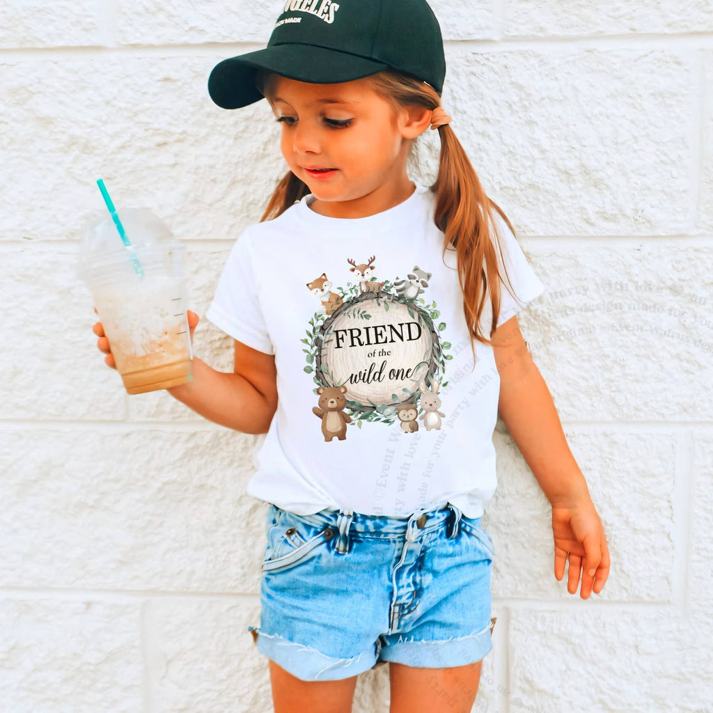 Girl in a ball cap holding a drink in a white Friend of the Wild One shirt.