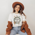 Smiling woman in a brown hat wearing a Mommy of the Wild One shirt with a woodland wreath.