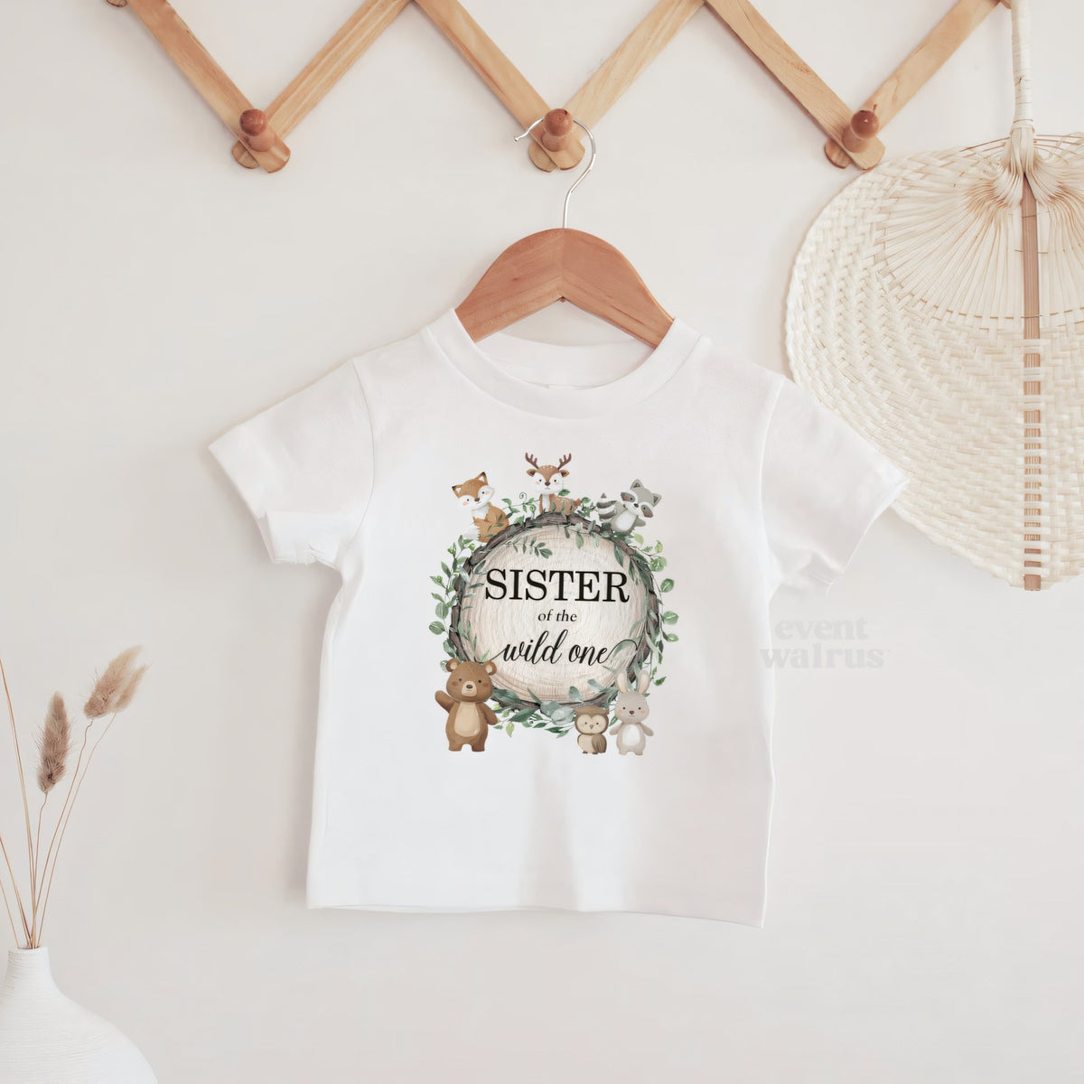 White Sister of the Wild One baby tee hanging on a wooden peg rail.