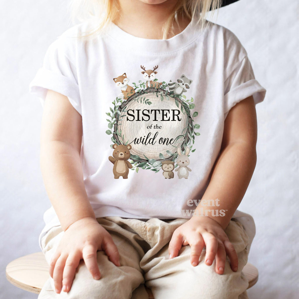 Toddler girl in a black hat sitting in a white Sister of the Wild One woodland tee.